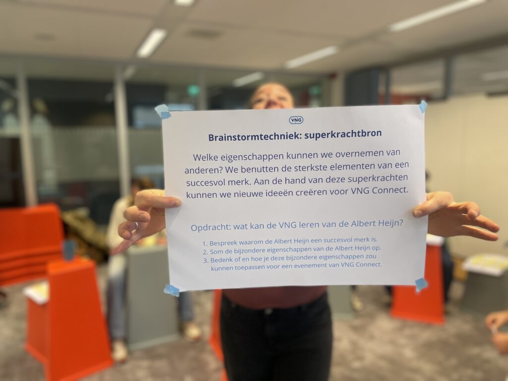 Communicatieadviseur Marloes houdt een vel papier voor zich met uitleg over de brainstormtechniek superkrachtbron. en een opdracht: wat kan de VNG leren van de Albert Heijn? 